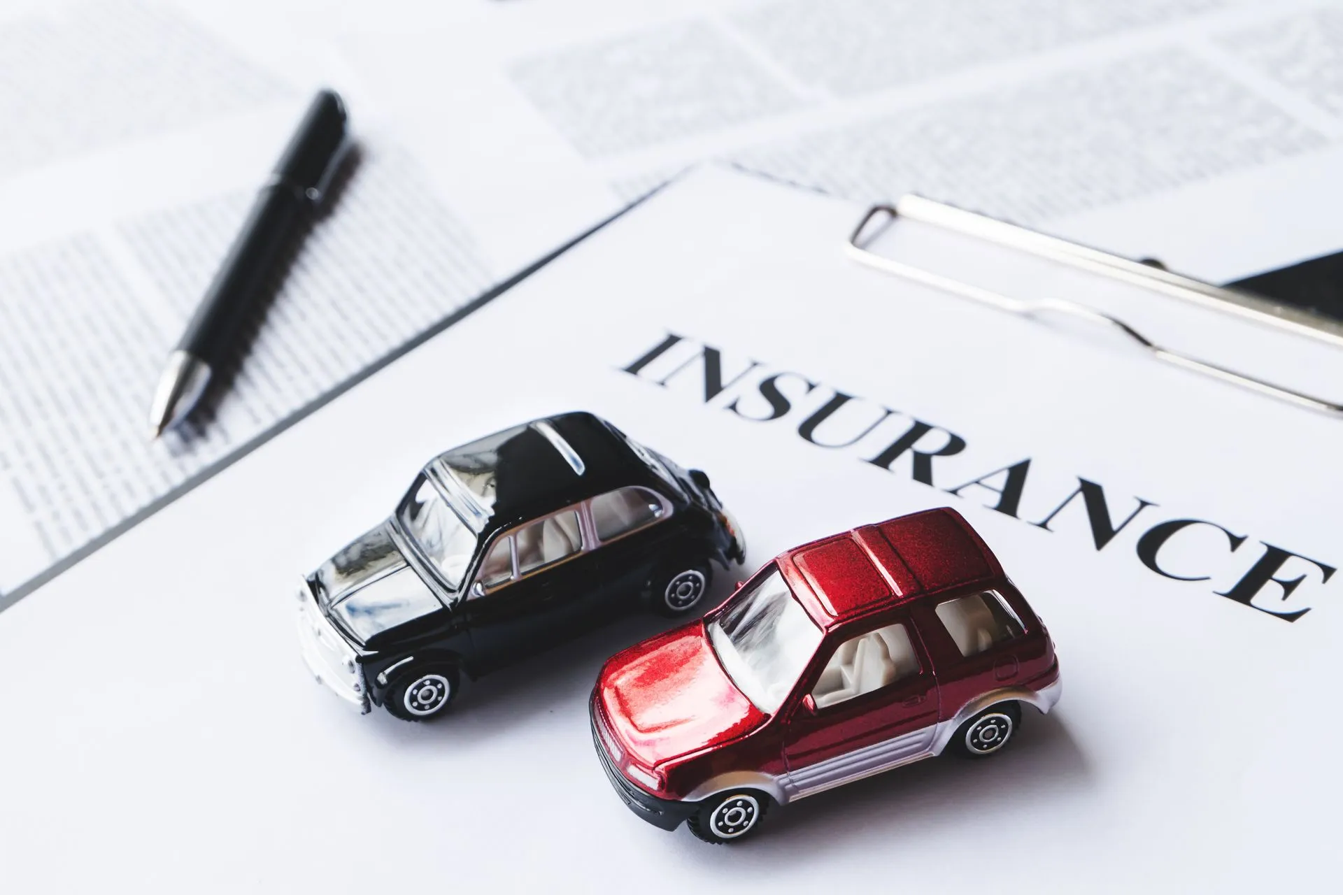 Two toy cars on top of an insurance document with a pen.