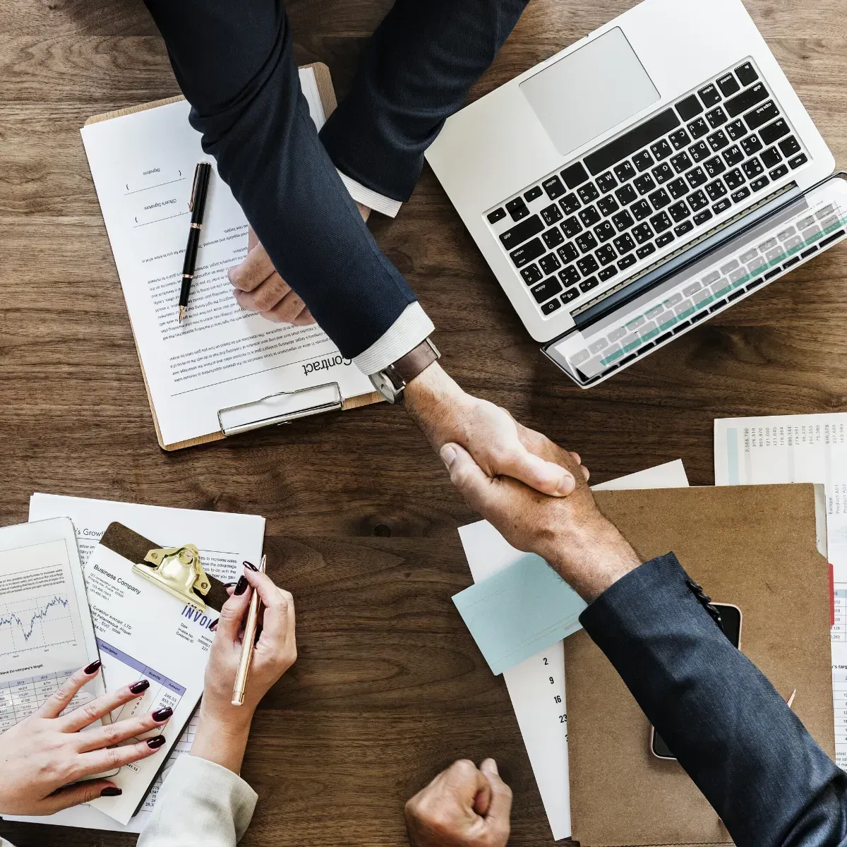 People shaking hands at a desk surrounded by documents.