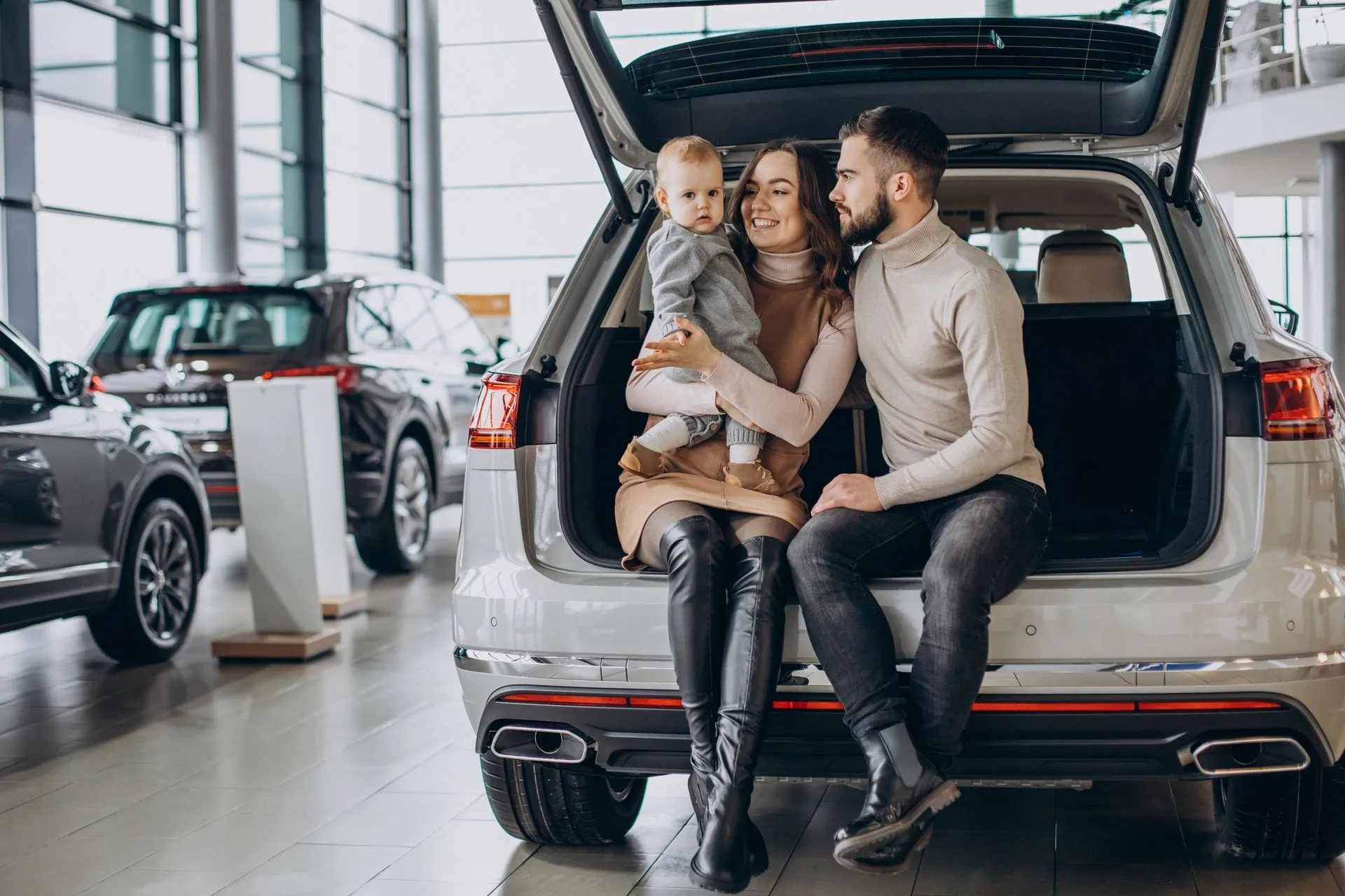 Family sitting in the open trunk of an SUV at a car dealership.