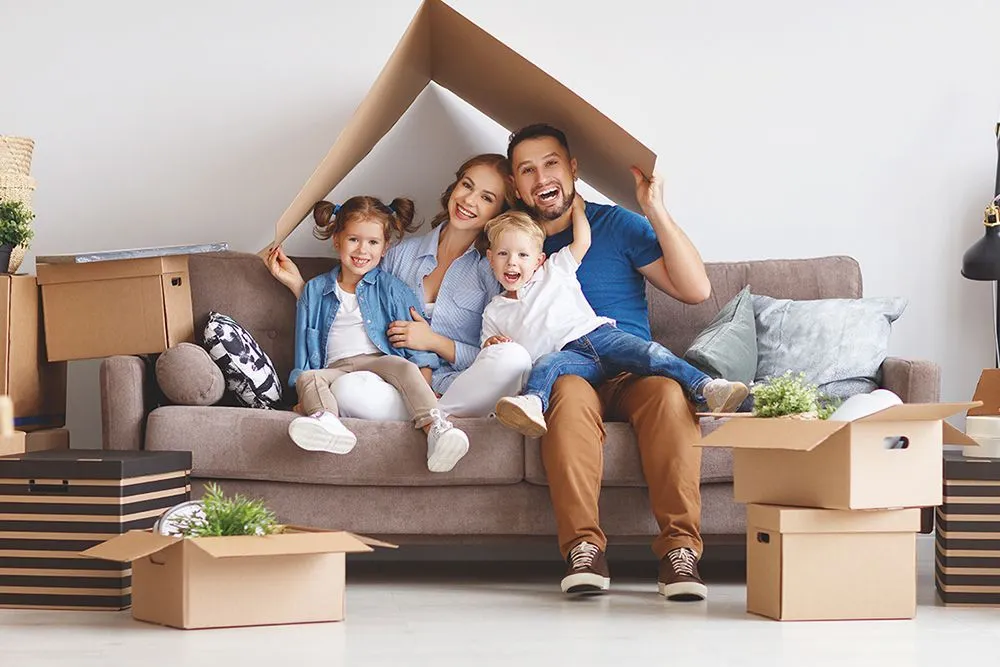 Family of four smiling under a cardboard house.