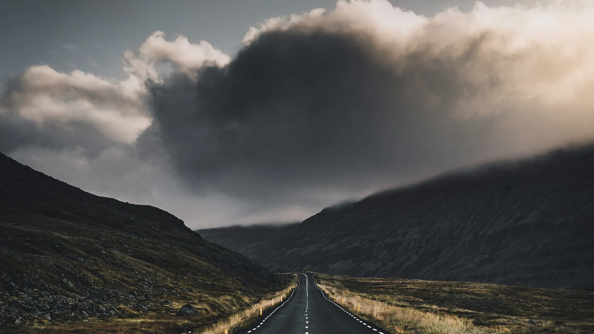 A long road stretching between dark hills under a cloudy sky.
